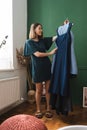 Young woman holding dresses on hanger, trying to decide what to wear.