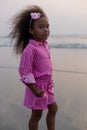 Charming dark-skinned girl with beautiful pink hair hoop looks at camera at sunset on beach.