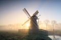 Charming Dutch windmill in fog at dawn