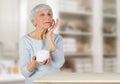 Charming elderly woman applying cosmetic cream on her face for facial skin care in bathroom at home