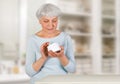 Charming elderly woman applying cosmetic cream on her face for facial skin care in bathroom at home.