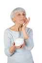 Charming elderly woman applying cosmetic cream on her face for facial skin care on a white background