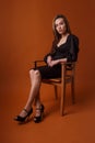 Pretty model in black dress, highheel shoes sits in chair on orange background Royalty Free Stock Photo