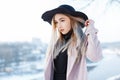 Charming elegant young woman in a vintage hat in retro style in a pink coat in a knitted dress stands on a warm winter day Royalty Free Stock Photo