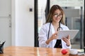 Female doctor in white uniform using digital tablet while sitting in modern medical office. Royalty Free Stock Photo