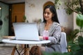 Charming female freelancer thinking about new ideas during work on laptop computer at outdoor cafe.