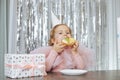 Charming, festively dressed red-haired baby 4-5 years old enjoys delicious cake for her birthday, sitting at table Royalty Free Stock Photo