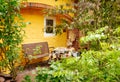 Charming front porch. Bench and table among the greenery on the background of a yellow wall