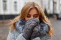 Charming funny young woman laughs and covers her face with her hands in knitted mittens on the background of vintage buildings