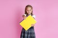 A charming girl with blond hair in a school uniform with a book in her hands on a pink background. Studio photo. Back to school