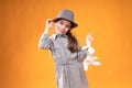 A charming girl in a hat tilting her head to the side holds a hat and a teddy hare in her hands smiling Royalty Free Stock Photo