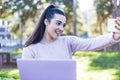 Charming girl with a laptop makes a selfie while sitting on a bench in the park Royalty Free Stock Photo