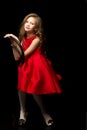 Charming girl in a red dress sits on a chair on a black background Royalty Free Stock Photo