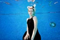 A charming girl is sitting underwater at the bottom of the pool in a black dress with white horns on her head on a sunny