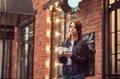 A charming girl wearing a leather jacket with a rucksack holding cup with takeaway coffee outside near the cafe. Royalty Free Stock Photo