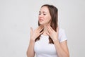 Charming girl in a white T-shirt on a gray background touches a throat that hurts a lot. Anguine disease Royalty Free Stock Photo