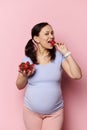 Charming glamour pregnant woman eating fresh sweet strawberries out of bowl, isolated on pink background. Pregnancy diet Royalty Free Stock Photo