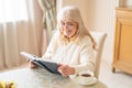 Smiling aged woman reading book over a cup of tea