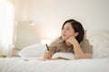 A happy Asian plus-size woman is daydreaming about her happiness while keeping her diary on her bed Royalty Free Stock Photo