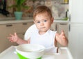 Charming happy baby boy in big white bib sitting in highchair and posing for the camera. Plate with food in front of the Royalty Free Stock Photo