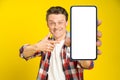 Charming happy man pointing at smartphone with white empty screen, wearing red plaid shirt and jeans cellphone display Royalty Free Stock Photo