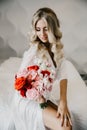 Beautiful blonde with a bouquet of flowers sits on a bed in a white room Royalty Free Stock Photo