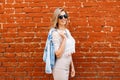 Charming happy young hipster woman with a beautiful smile in a white lace blouse in a denim jacket in black sunglasses in a beige Royalty Free Stock Photo