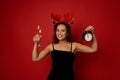 Charming Hispanic woman wearing antler hoop and black velvet dress holding an alarm clock and champagne flute with sparkling wine