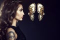 Charming lady with dark wavy silky hair wearing jewel crown and looking in the face of Venetian mask hanging in the air
