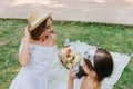 Charming lady in white dress posing with pleasure beside picnic basket while her daughter making photo. Dark-haired Royalty Free Stock Photo