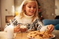 Charming little blonde girl taking delicious cookie from plate w