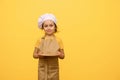 Charming adorable kid girl 6 years old, little chef pastry, smiles cutely and holds out at camera a wooden board Royalty Free Stock Photo