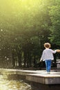 Ufa, Russia - July 31, 2013:little child walking along the edge of the fountain, holding his hand on the background of green trees