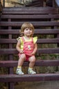 Charming little girl baby sitting on the wooden stairs in a beautiful dress while walking in Lviv Royalty Free Stock Photo