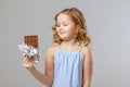 Charming little girl child blonde looks at a bar of chocolate. Gray background, studio, portrait Royalty Free Stock Photo