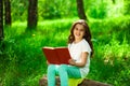 Charming little girl in forest with book sitting on tree stump Royalty Free Stock Photo