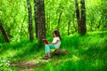 Charming little girl in forest with book sitting on tree stump Royalty Free Stock Photo