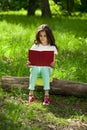 Charming little girl in forest with book sitting on tree stump Royalty Free Stock Photo