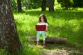 Charming little girl in forest with book sitting on tree stump Royalty Free Stock Photo