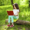 Charming little girl in forest with book sitting on tree stump Royalty Free Stock Photo