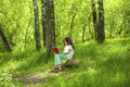 Charming little girl in forest with book sitting on tree stump Royalty Free Stock Photo