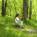 Charming little girl in forest with book sitting on tree stump