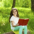 Charming little girl in forest with book sitting on tree stump Royalty Free Stock Photo