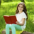 Charming little girl in forest with book sitting on tree stump Royalty Free Stock Photo