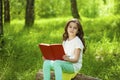 Charming little girl in forest with book sitting on tree stump Royalty Free Stock Photo