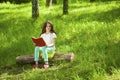 Charming little girl in forest with book sitting on tree stump Royalty Free Stock Photo