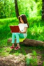 Charming little girl in forest with book sitting on tree stump Royalty Free Stock Photo