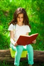 Charming little girl in forest with book sitting on tree stump Royalty Free Stock Photo