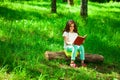 Charming little girl in forest with book sitting on tree stump Royalty Free Stock Photo