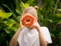 Charming little girl with fresh papaya. Caucasian girl holding slice of papaya fruit in front of her eye. Selected focus. Green
